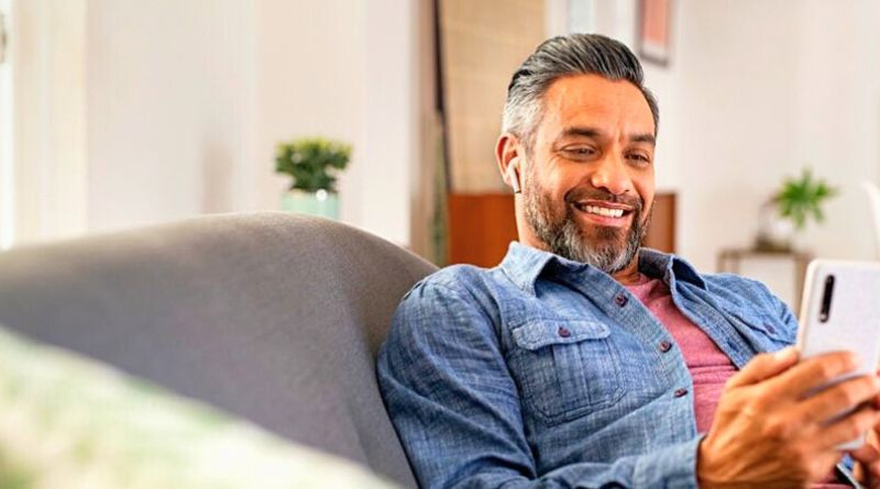 Imagem de homem adulto feliz usando smartphone impactado por marketing digital sentado no sofá.
