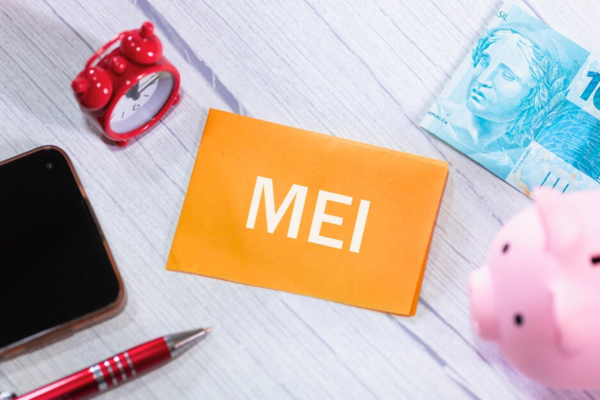 A sigla MEI para Microempreendedor Individual em português brasileiro escrita em um pedaço de papel sobre uma mesa de madeira